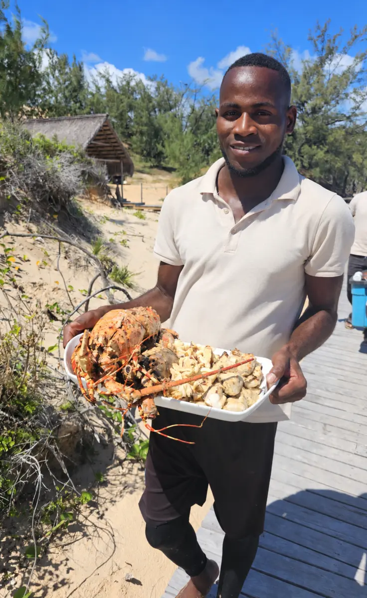 Baobab Journeys guest holding a platter of freshly prepared lobster and seafood on a tropical island boardwalk in the Bazaruto Archipelago, Mozambique.